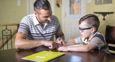 Jeune qui fait ses devoirs aidé d'un adulte